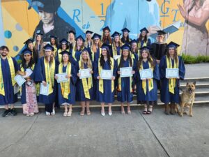Graduates of the Vet Tech Program holding their diplomas in front of a painted mural.