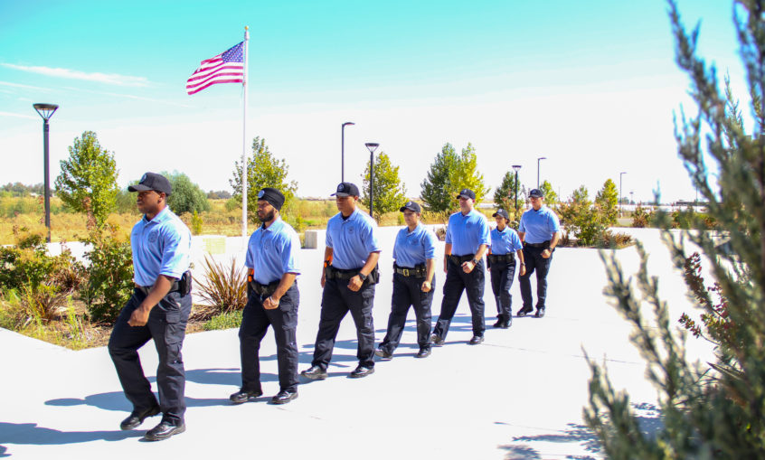 Photo of trainees walking on sidewalk with American flag in the background