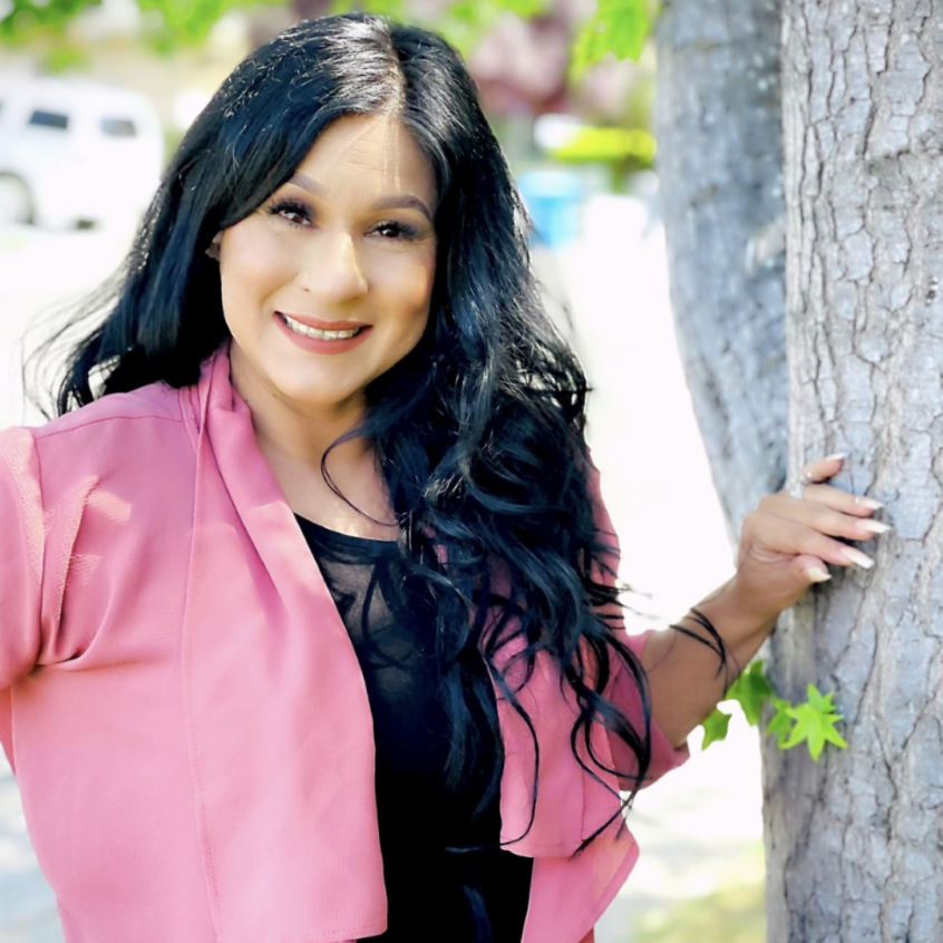 Silvia Gonzalez in a pink jacket with her left hand on a tree
